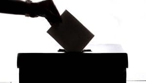 an shadowed arm dropping a ballot into a voting box