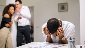 Black man with his head in his hands being bullied by 2 people behind him