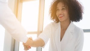 A woman of colour clasping a hand with another person representing the sealing of a deal