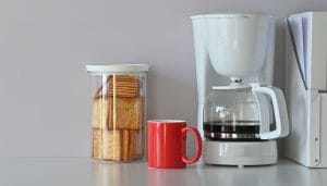 close up of a coffee pot, crackers and a red coffee mug on a table