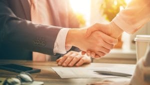 A business handshake between two people; a man and a woman. The photo is shot from a low angle, focusing on the hands of the people shaking hands suggesting a successful business meeting.